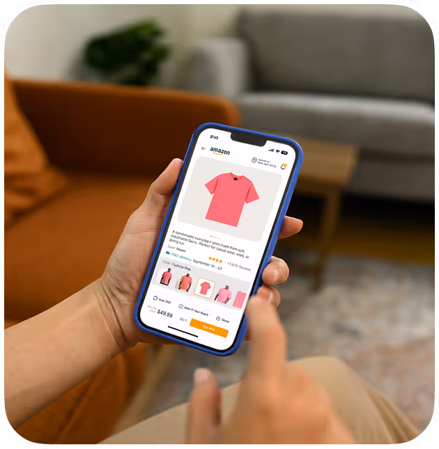 Person holding a smartphone showing an Amazon product page for a pink t-shirt with price and color options.